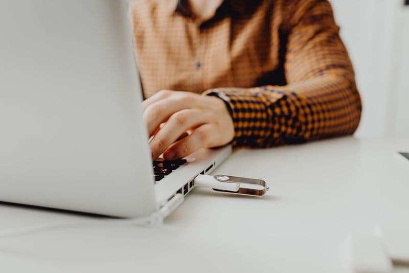 Antivírus para home office: vale a pena investir? A person working on a laptop with a USB flash drive connected, representing technology and data storage.