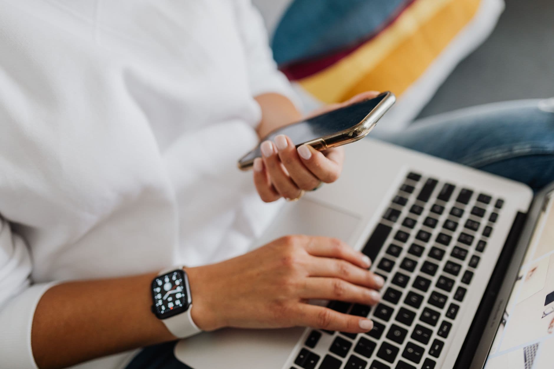 Banco de horas no home office: como funciona Close-up of a person using a smartphone and laptop for work, showcasing multitasking in a modern home office setting.
