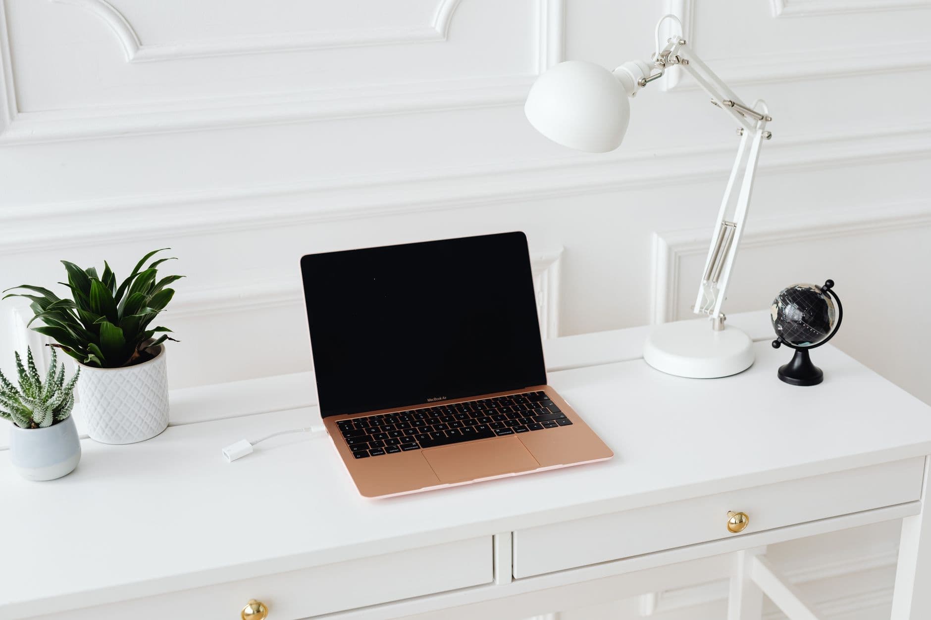 Burnout de freelancer: como evitar o esgotamento no trabalho Clean and stylish workspace featuring a laptop, desk lamp, and potted plants on a white desk.