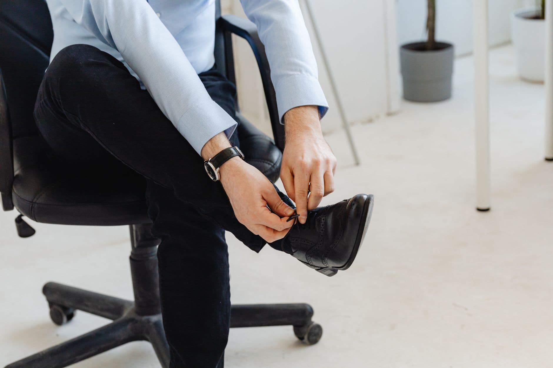 Cadeira ergonômica para home office vale a pena? Person in smart casual attire, indoors, tying shoelaces, creating a business-ready look.