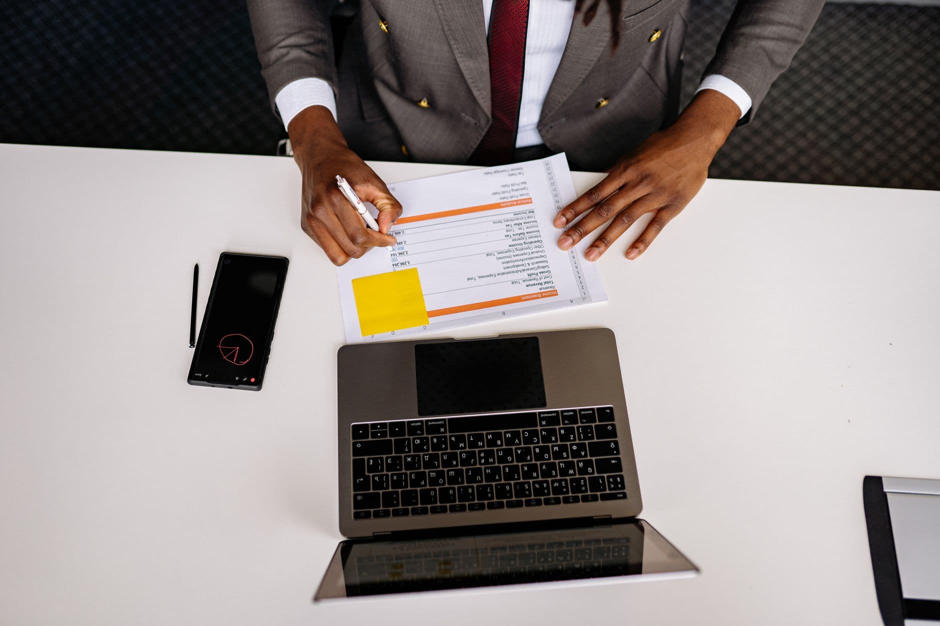 Carreira internacional totalmente remota: passo a passo Top view of a business professional analyzing documents with a laptop on a white desk in an office setting.