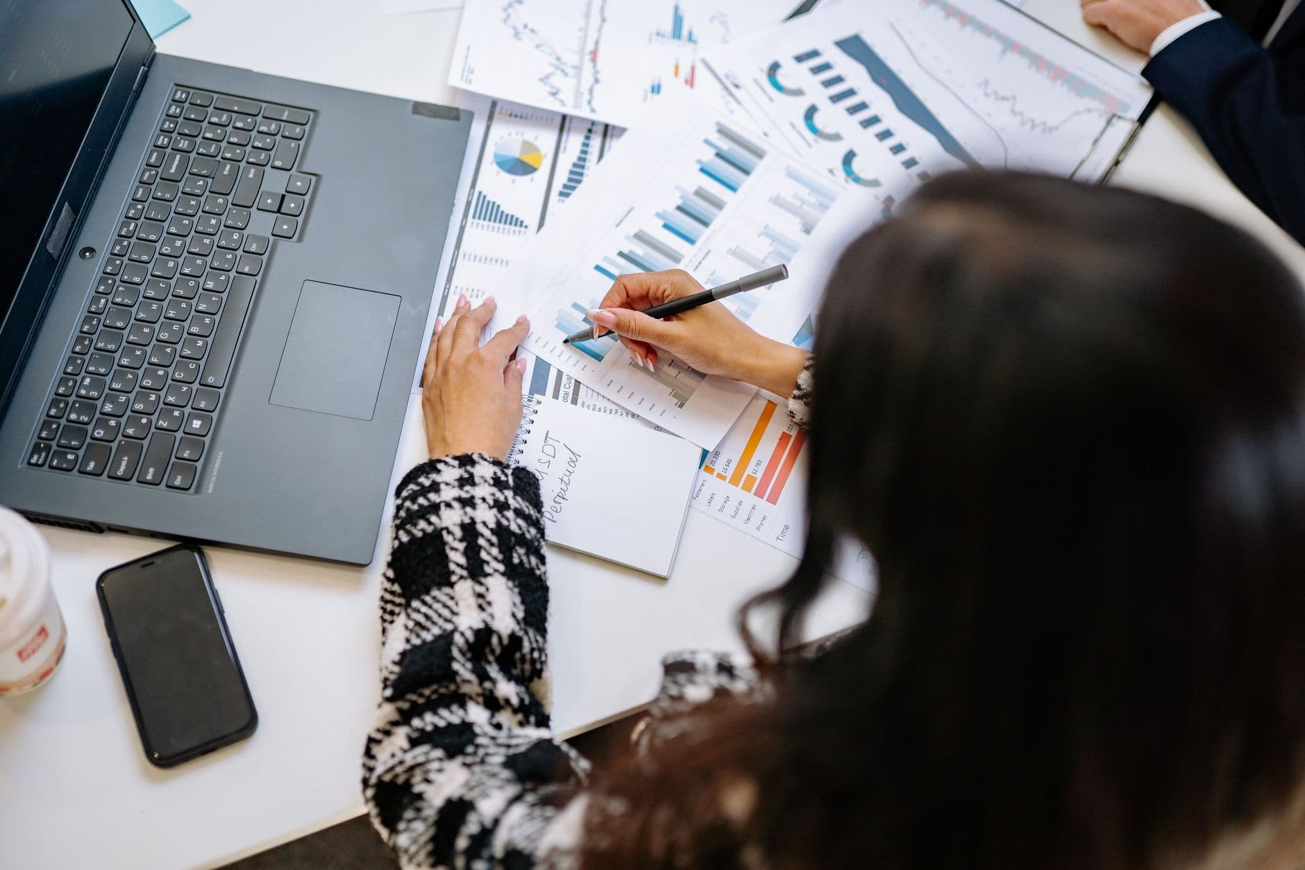 Como abrir MEI para trabalhar como freelancer remoto A professional woman reviewing financial charts and graphs with a laptop and smartphone on the desk.