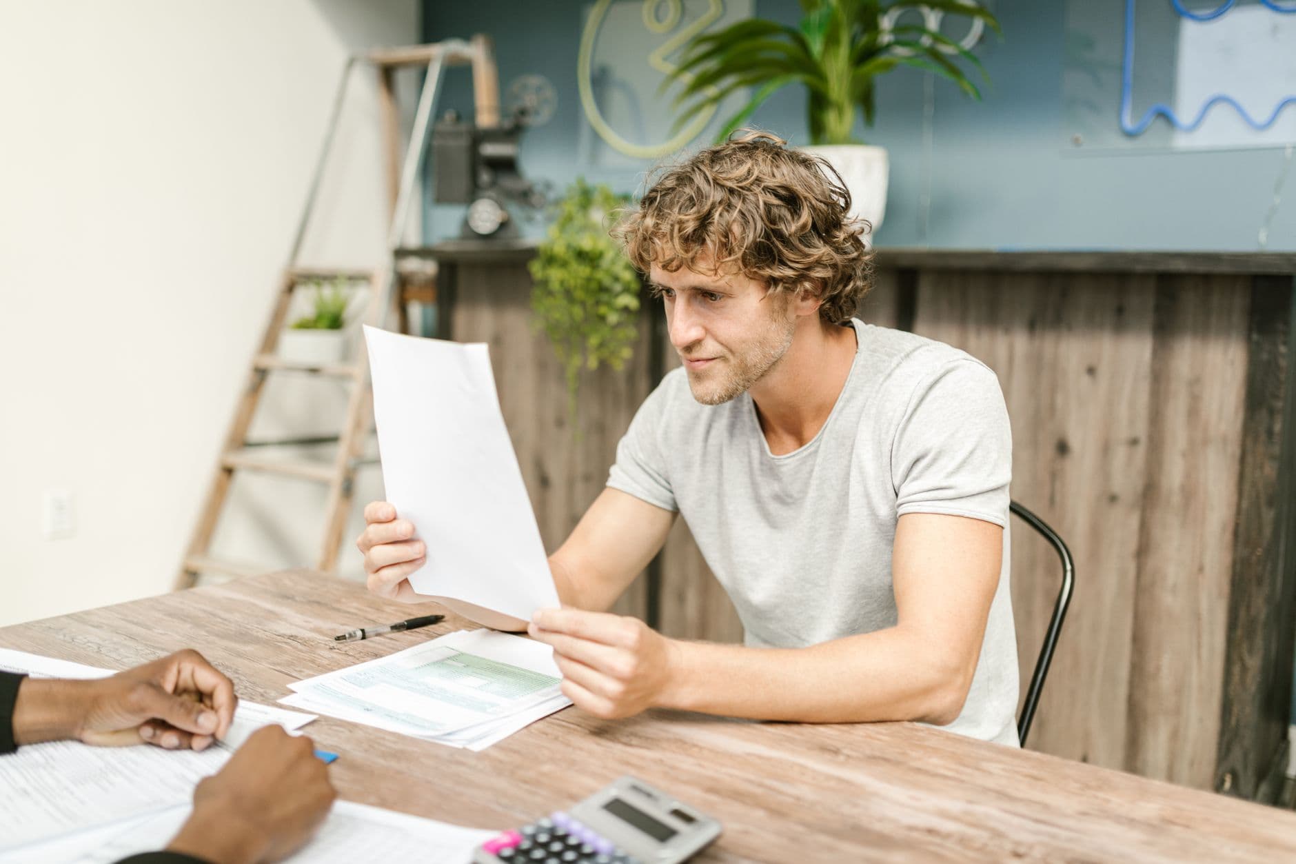 Como cobrar adiantado sendo freelancer A man with curly hair evaluates documents at a desk, highlighting focused work in a professional setting.