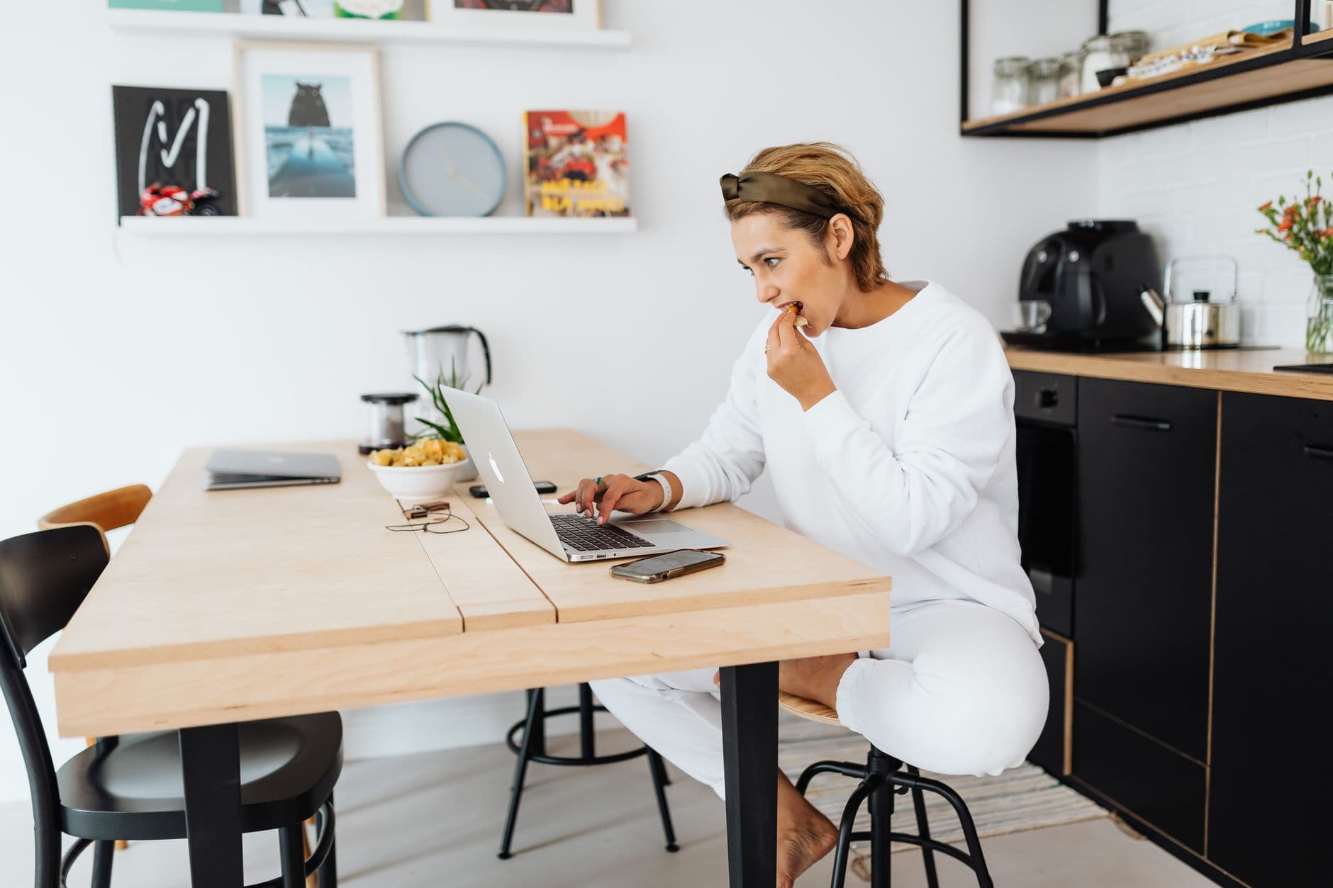 Como começar bem o dia trabalhando de casa Casually dressed woman working on a laptop at home in a modern kitchen setting.