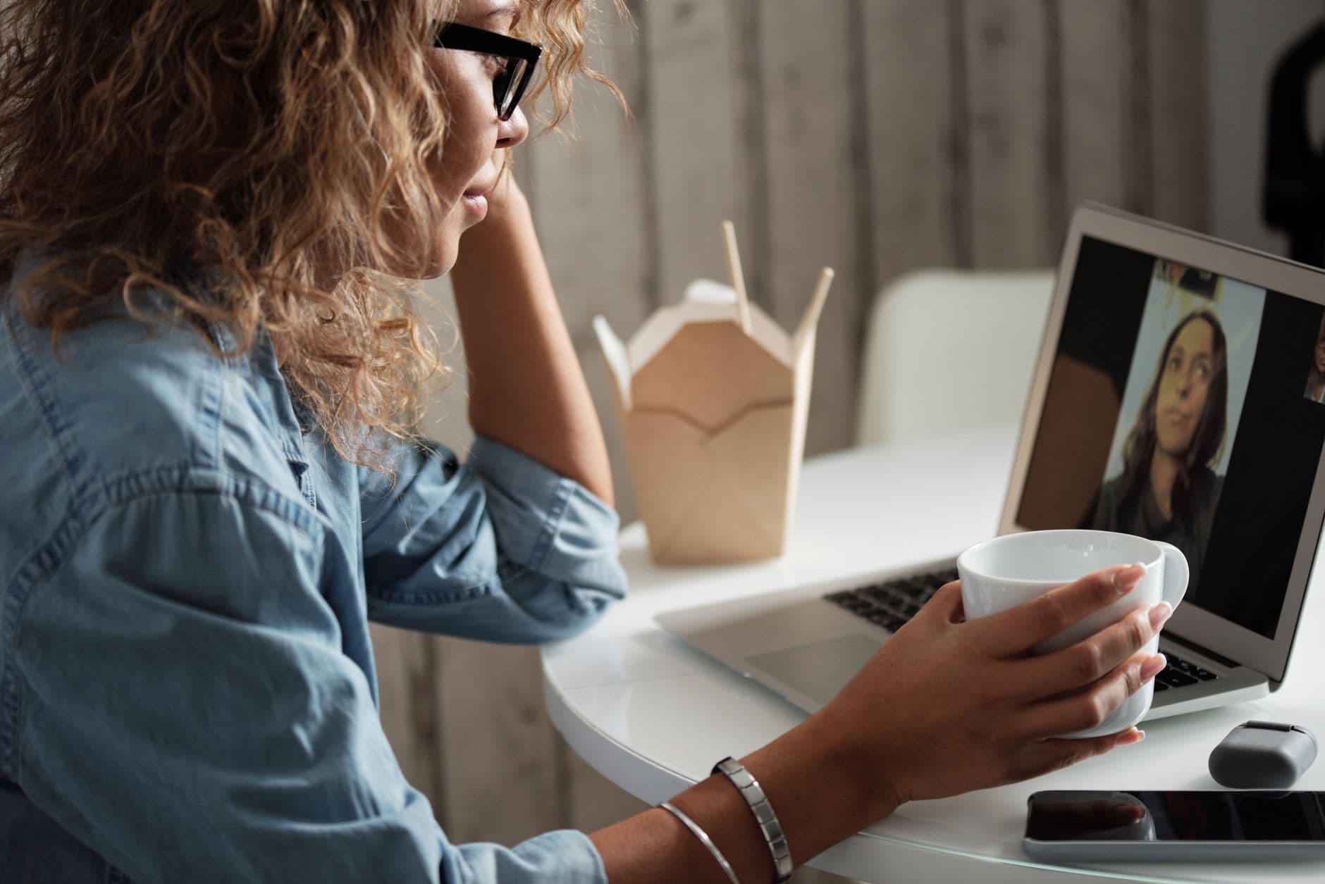 Como conseguir um emprego remoto: passo a passo Woman relaxing with a coffee while on a video call using her laptop indoors.