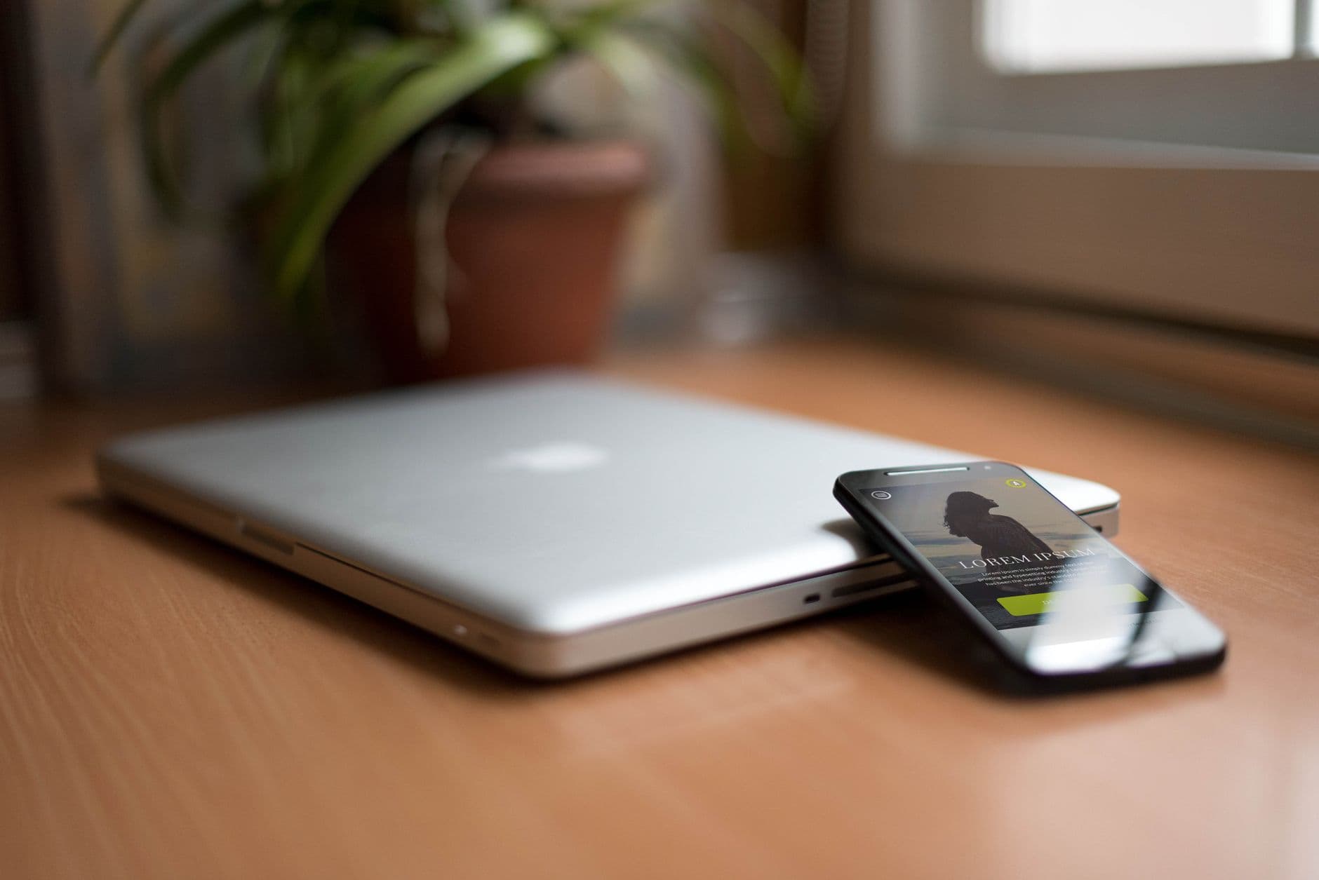 Como evitar distração trabalhando de casa Close-up of a silver laptop and smartphone on a wooden desk, capturing modern work essentials.