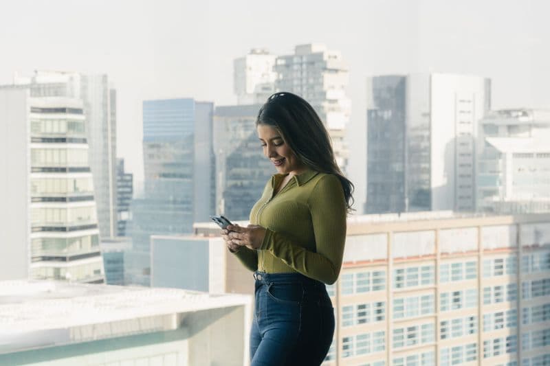 Como lidar com quedas de energia no trabalho remoto Woman looks at smartphone inside high-rise building with cityscape in background.