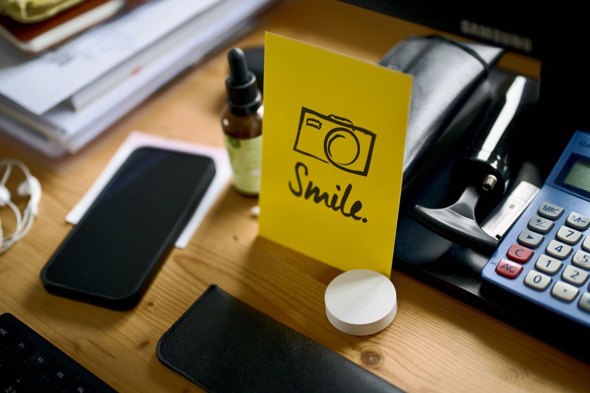 Como montar um home office gastando pouco A desk with a smartphone, calculator, and motivational card displaying the word 'Smile'.