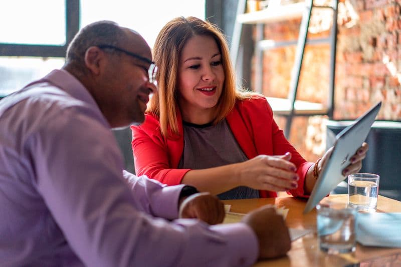 Como negociar prazo de entrega sendo freelancer Two adults engaged in a productive conversation using a tablet in a modern office setting.