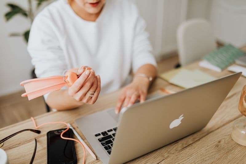 Como organizar a mesa de trabalho no home office Woman using a laptop at a wooden desk with various accessories and a smartphone.