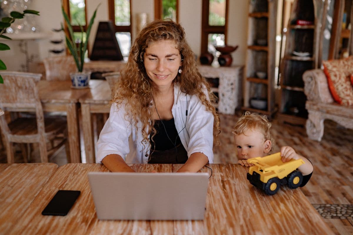 Pessoa trabalhando no laptop enquanto crianças fazem atividades em casa