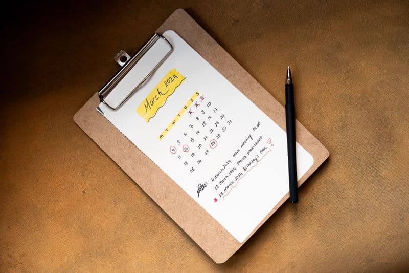 Como organizar o trabalho remoto com filhos de férias Top view of a March 2024 calendar on a clipboard with a pen, ideal for planning or scheduling content.
