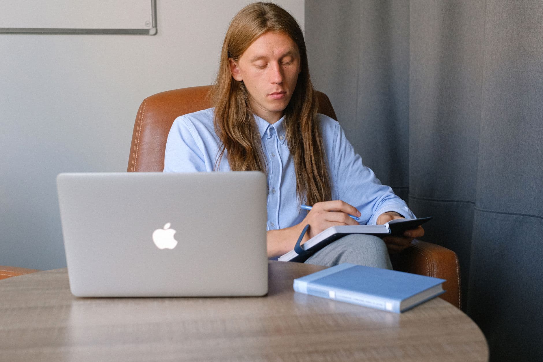 Como pedir aumento trabalhando remoto Pensive worker in shirt sitting on chair and taking notes in notebook while browsing laptop in room in daytime