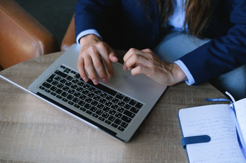 Como pedir referências trabalhando remoto From above crop anonymous freelancer in stylish clothes sitting at table with opened notebook and working on project on laptop