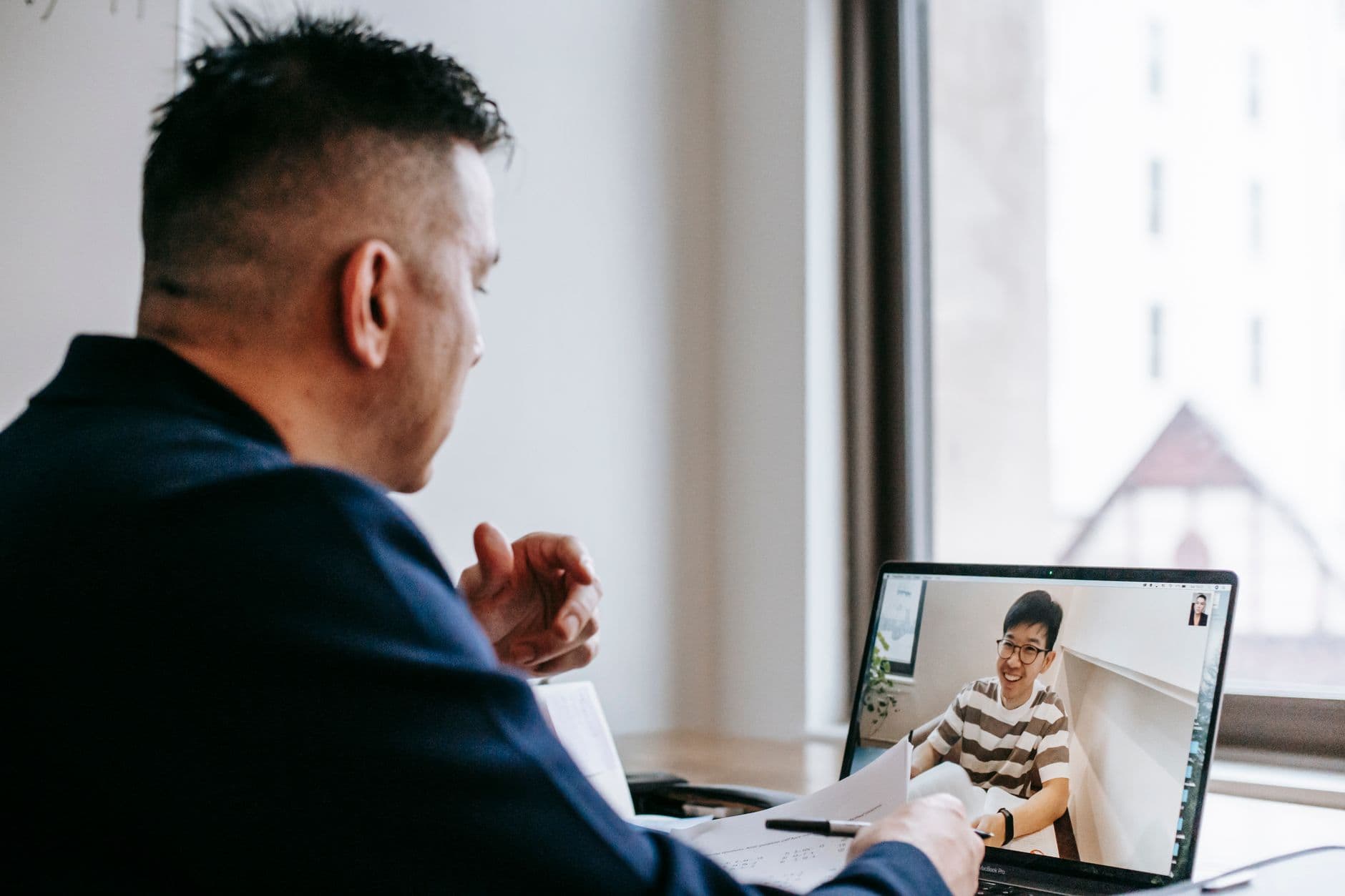 Profissional trabalhando em laptop enquanto participa de uma conversa por vídeo em casa
