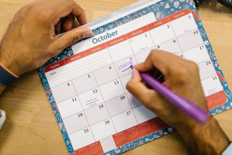 Pessoa anotando compromisso em um calendário de papel com caneta roxa