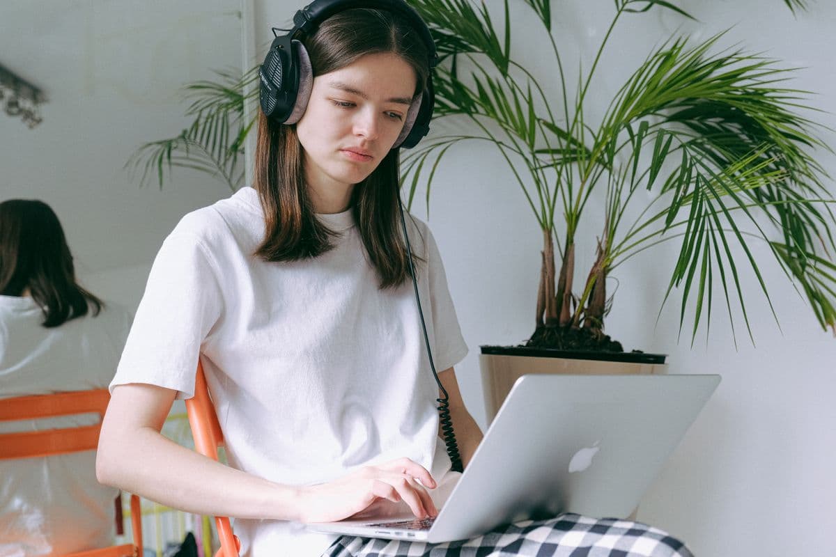 Pessoa trabalhando em um laptop em uma mesa de home office com fones de ouvido e ambiente organizado.