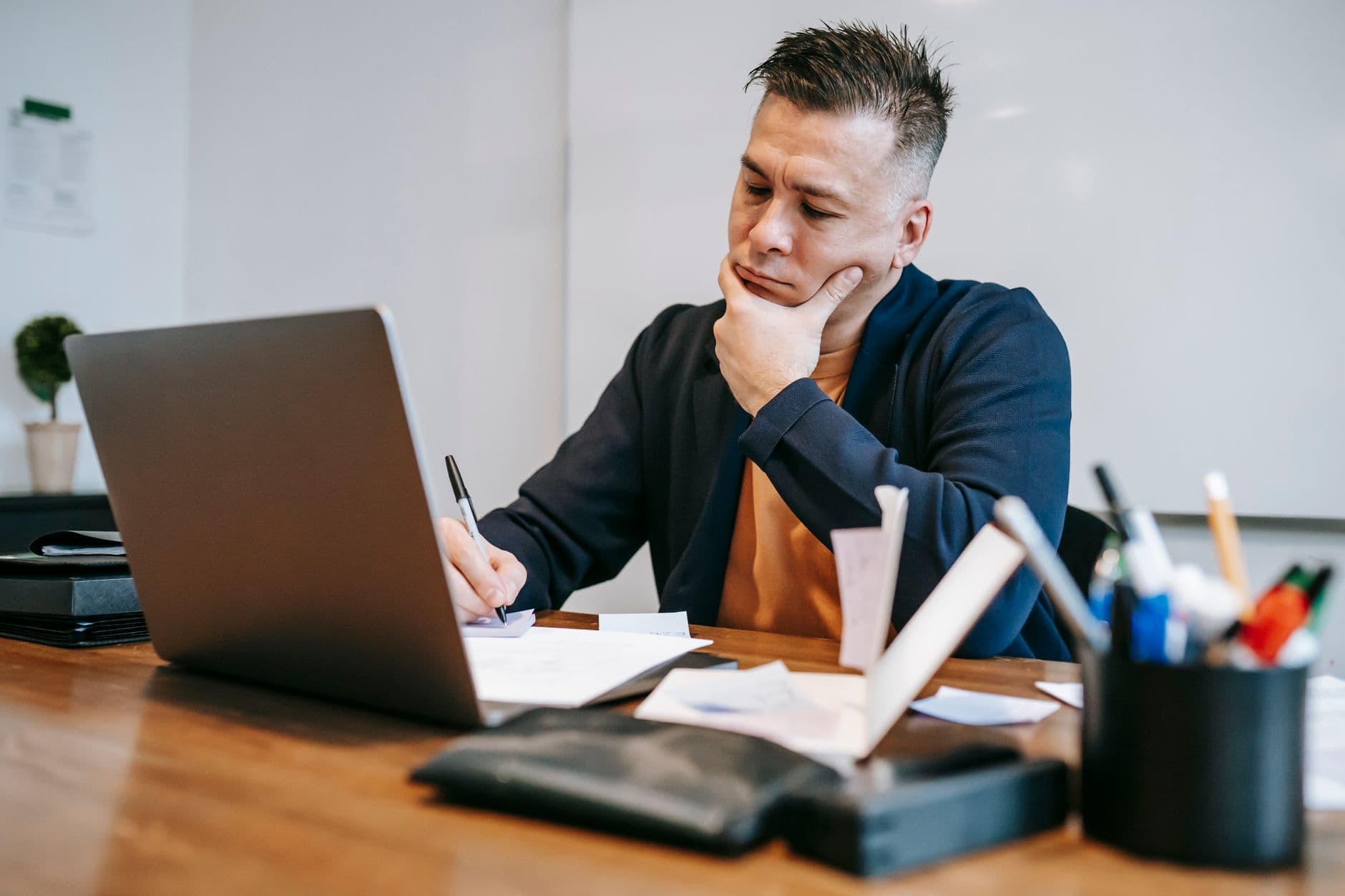 Como usar IA para produtividade no home office Concentrated man working on laptop and taking notes at a wooden desk in a home office.