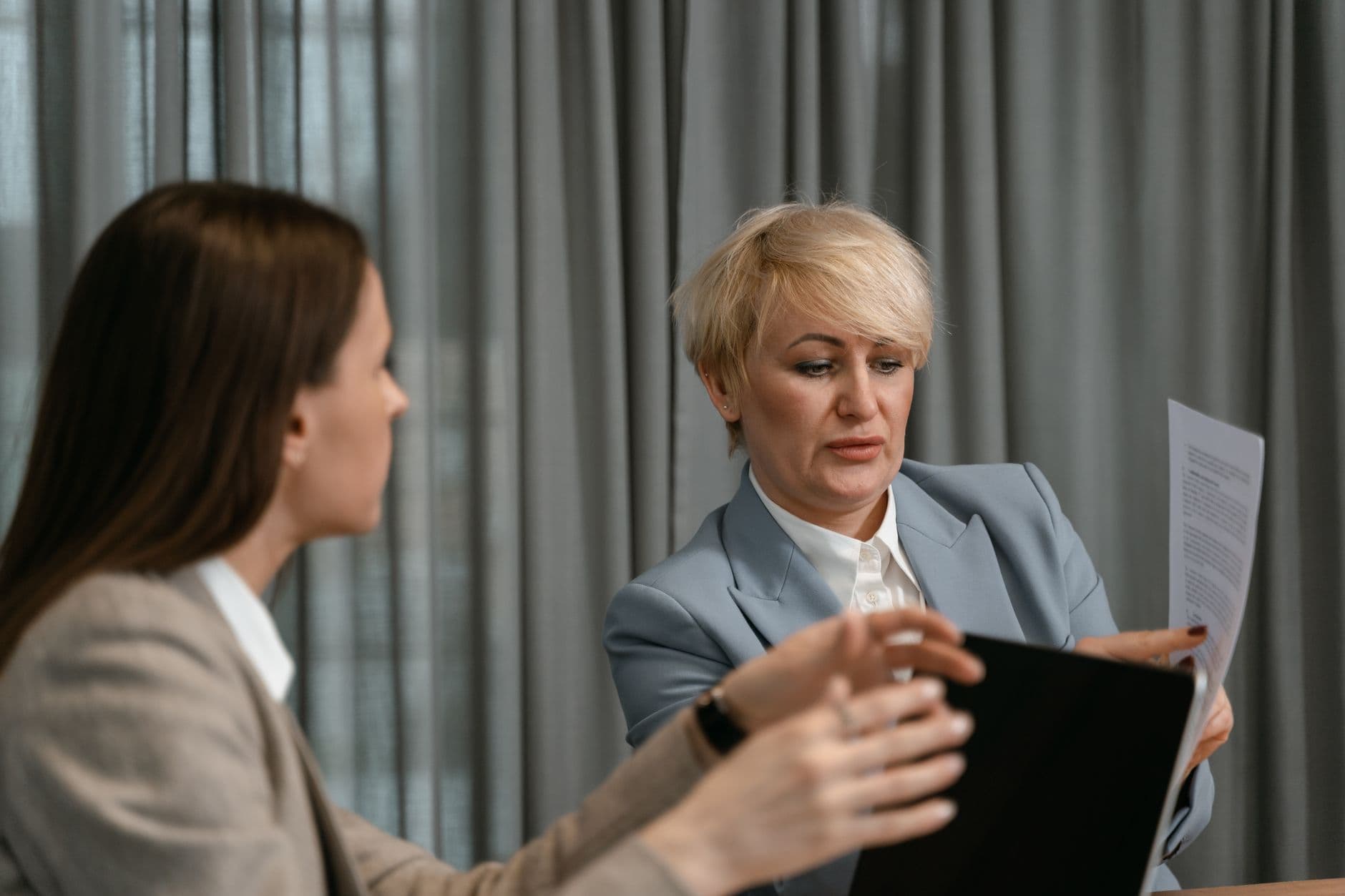 Como validar um cliente antes de fechar contrato remoto Two women discussing documents in a corporate meeting.