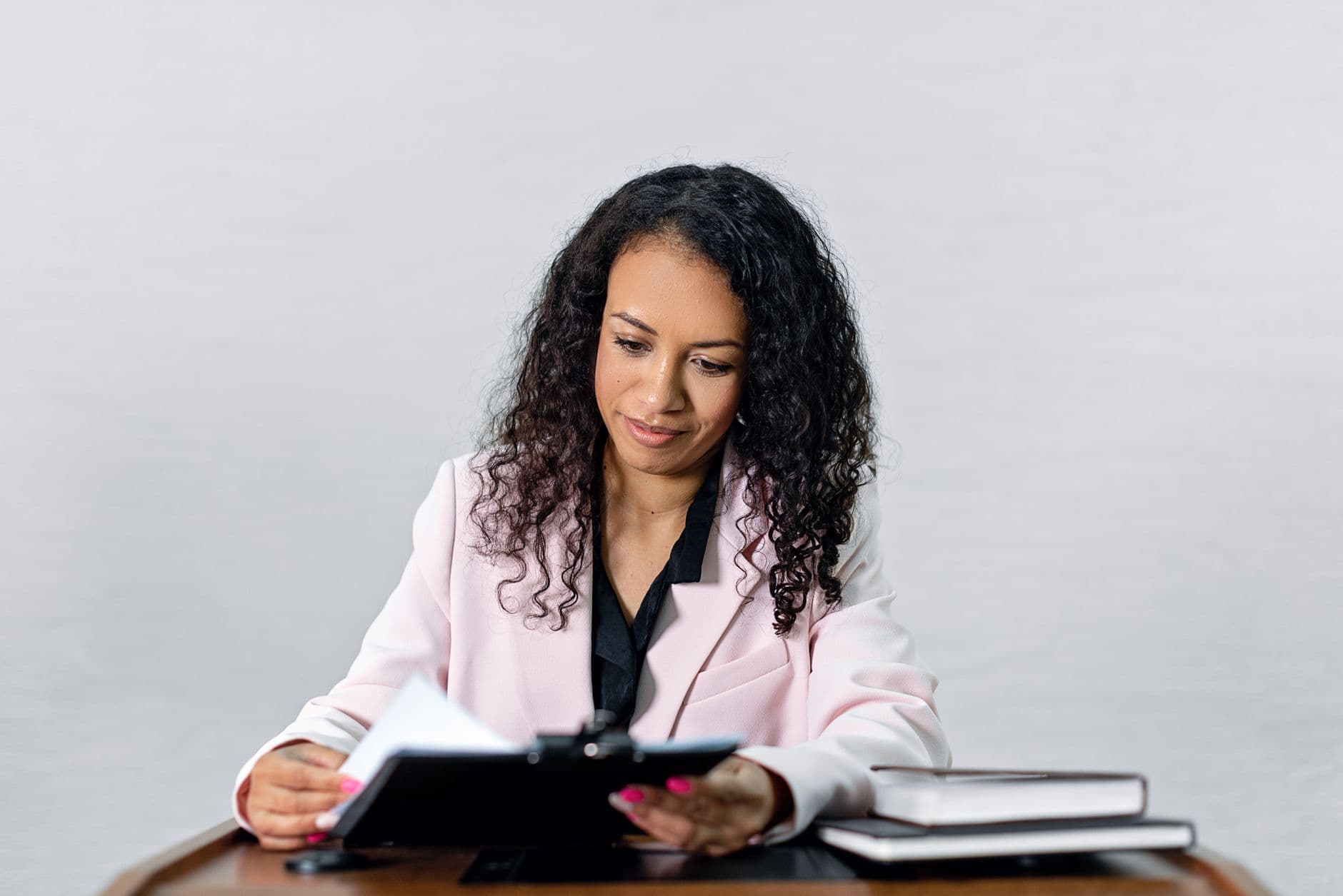Como Construir Autoridade no LinkedIn Trabalhando Remoto Confident woman with curly hair in a formal attire reviewing documents at a desk.