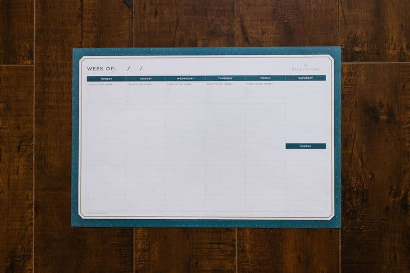 Creche e home office: como conciliar a rotina Top view of a blank weekly planner on a wooden surface, perfect for organizing your week.