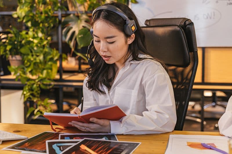 Deep work no home office: proteja seu foco Professional Asian woman with headset taking notes at a desk in an office setting.