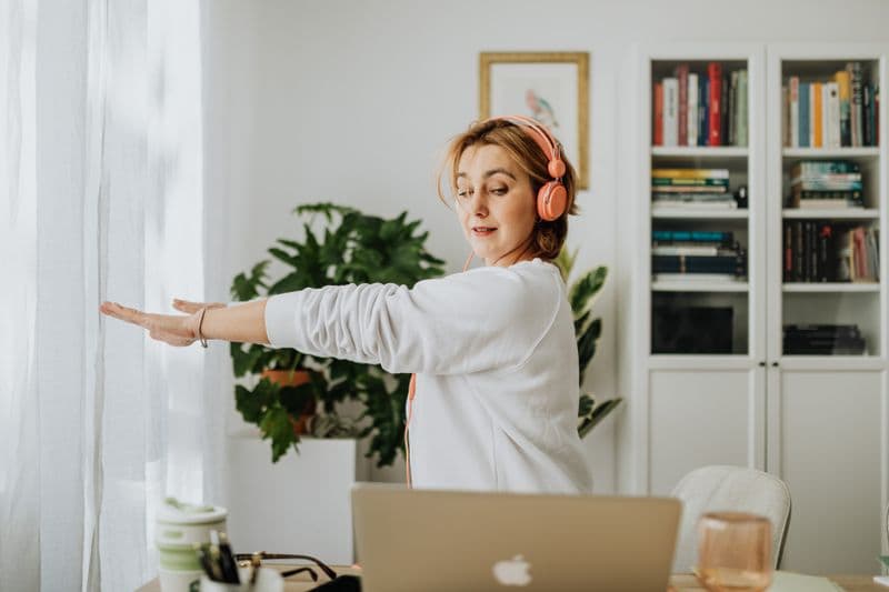 Dor lombar no home office: causas e ajustes Woman exercising with headphones in a cozy home office setting. Lifestyle and wellness focus.