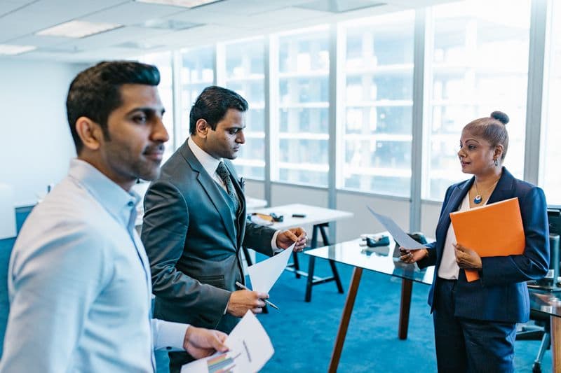 Quanto uma empresa economiza com home office Business professionals discussing documents in a modern office environment.