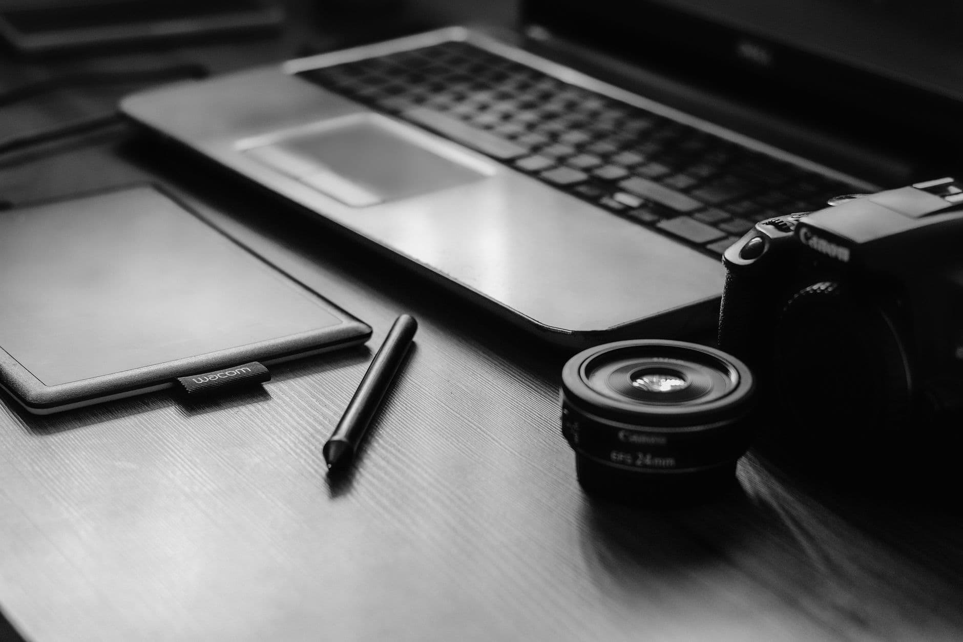 Entrevista de emprego remota: como se preparar A monochromatic workspace with a camera, laptop, lens, and tablet, ideal for photographers.