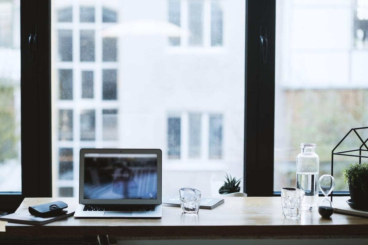Mesa de home office com notebook da empresa, copo d'água e janela ao fundo