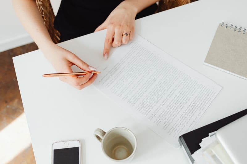 Ferramentas gratuitas de assinatura de documentos Close-up of a woman reviewing a document at a white desk with a pen.