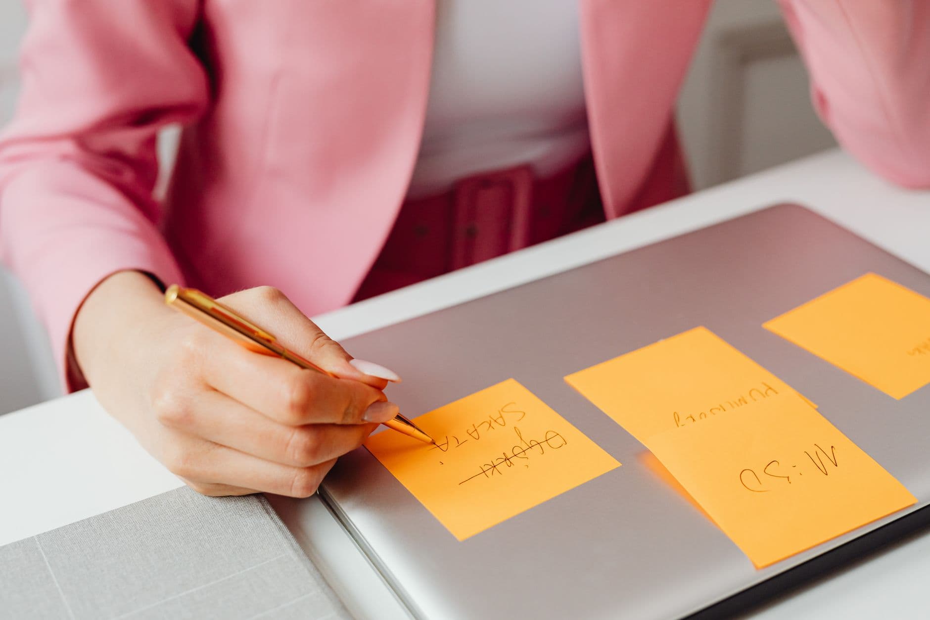 Ferramentas de gestão de projetos comparadas A woman writes on sticky notes placed on a laptop in an office setting.