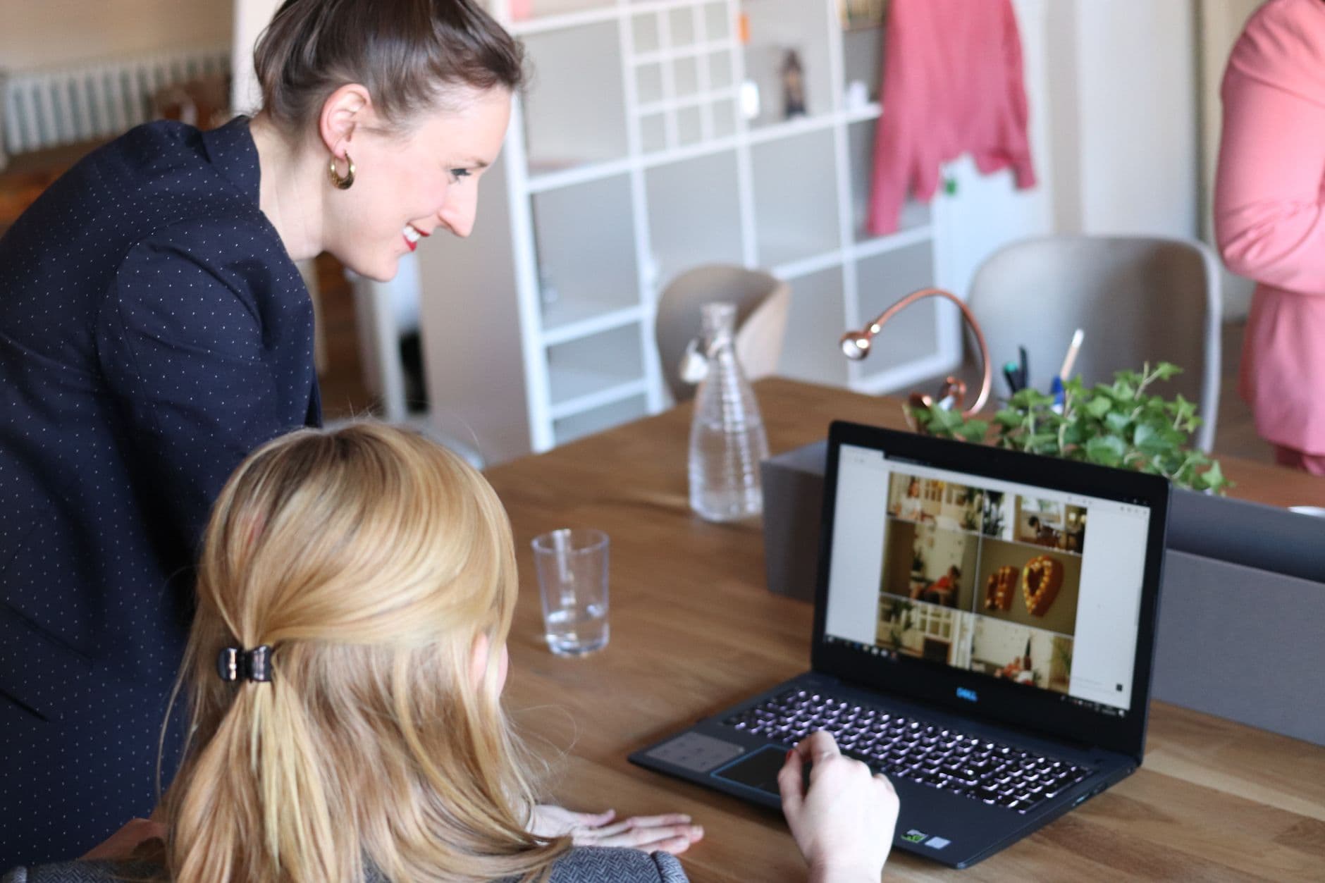 Fiverr: como começar do zero e conseguir pedidos Two women working together on a laptop in a stylish office setting.