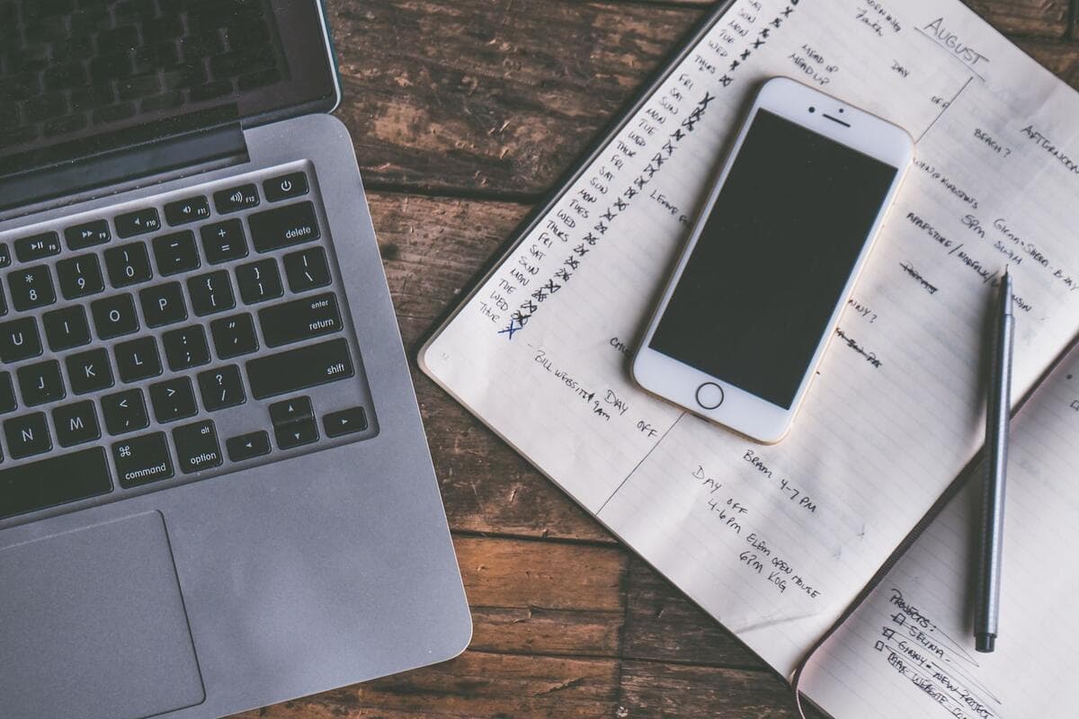 Como reduzir o silêncio nas próximas propostas Mesa de trabalho vista de cima com notebook, celular e caderno de anotações