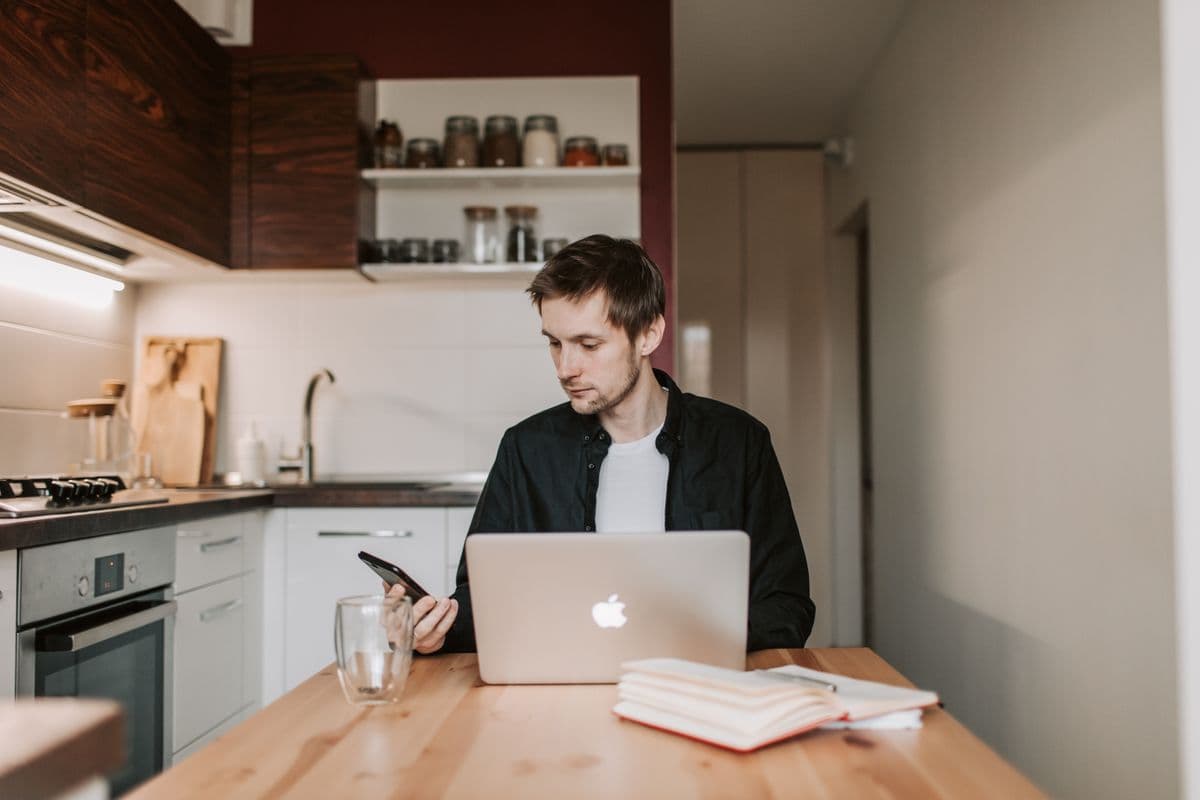Freelancer responde mensagens de clientes em um notebook ao lado de um celular em um home office.