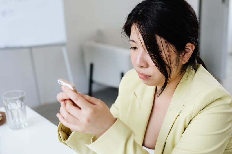Freelancer de atendimento no WhatsApp: como começar Focused woman in yellow blazer texting on smartphone at the office table.