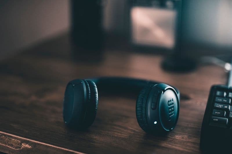 Editor de podcast freelancer: como entrar no mercado Close-up of wireless headphones placed on a wooden desk in dim lighting.