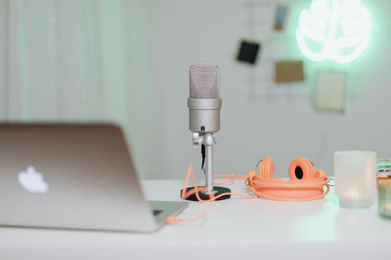 Freelancer de legendagem: como começar e cobrar A modern desk setup featuring a condenser microphone, laptop, and headphones in a stylish workspace.