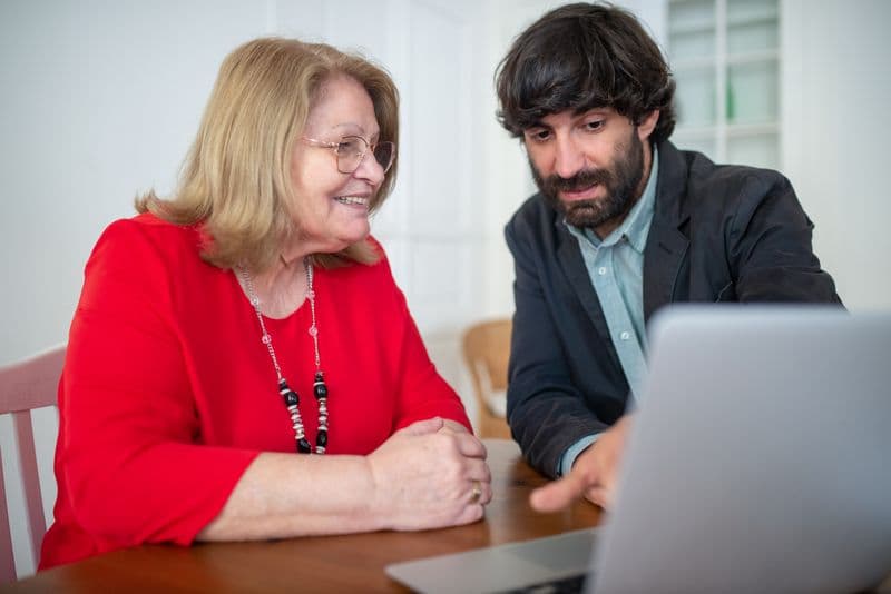 Freelancer de SEO: como vender o serviço e mostrar resultados A man and senior woman discuss work on a laptop indoors, focusing on technology and consulting.
