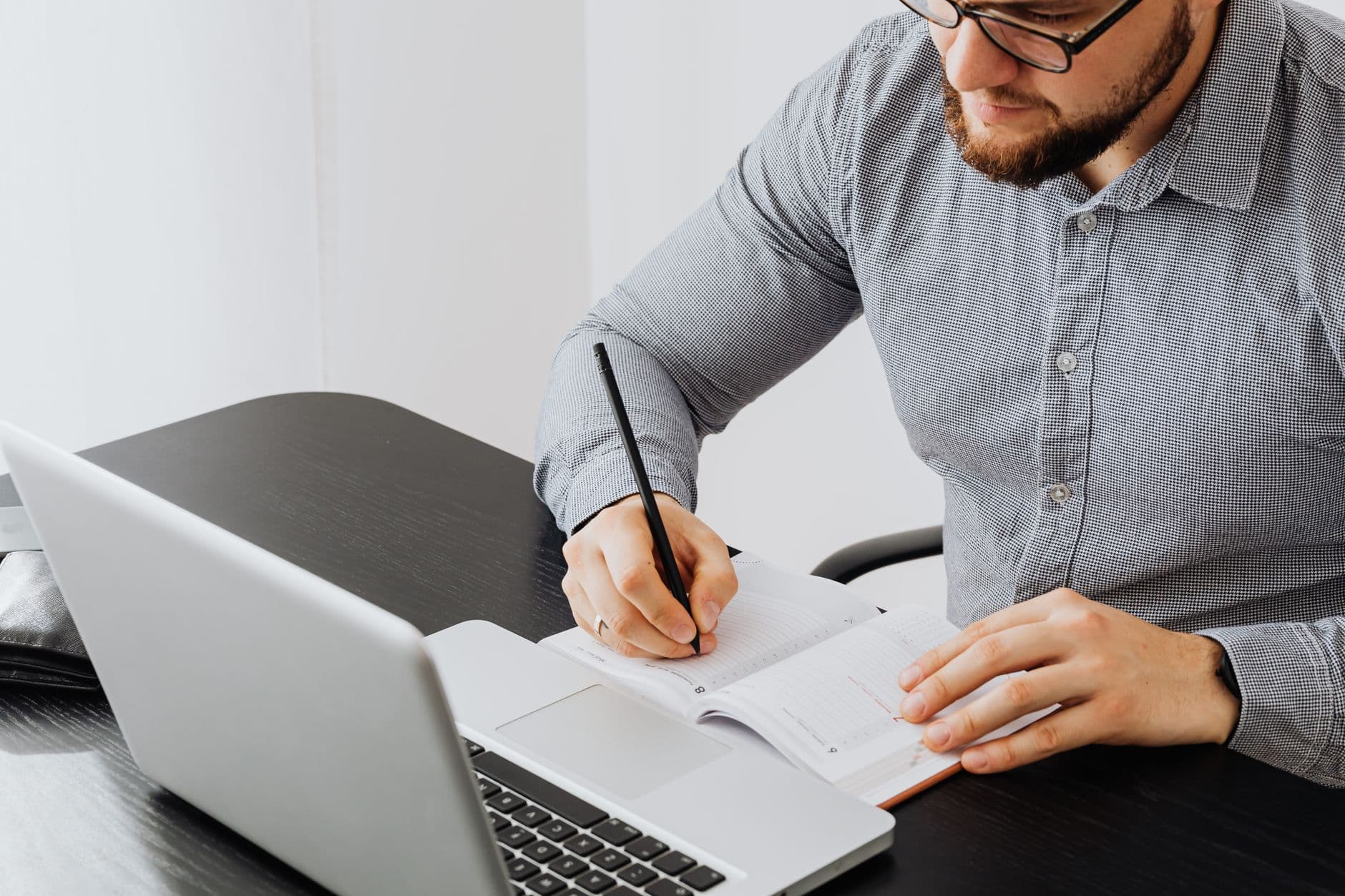 Freelancer pode ter carteira assinada ao mesmo tempo? Adult man working with laptop and writing in notebook at a modern indoor office.