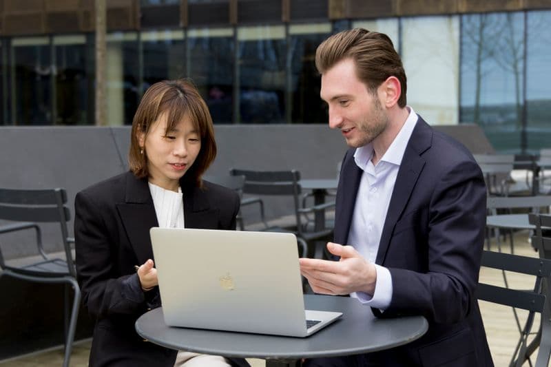 Freelancer programador: como começar do zero Two professionals collaborating over a laptop during an outdoor business meeting.
