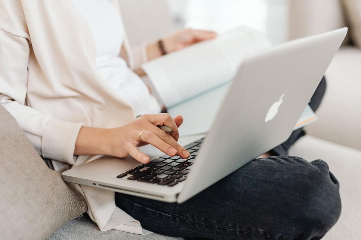 Pessoa digitando no notebook com um livro no colo, trabalhando com tradução