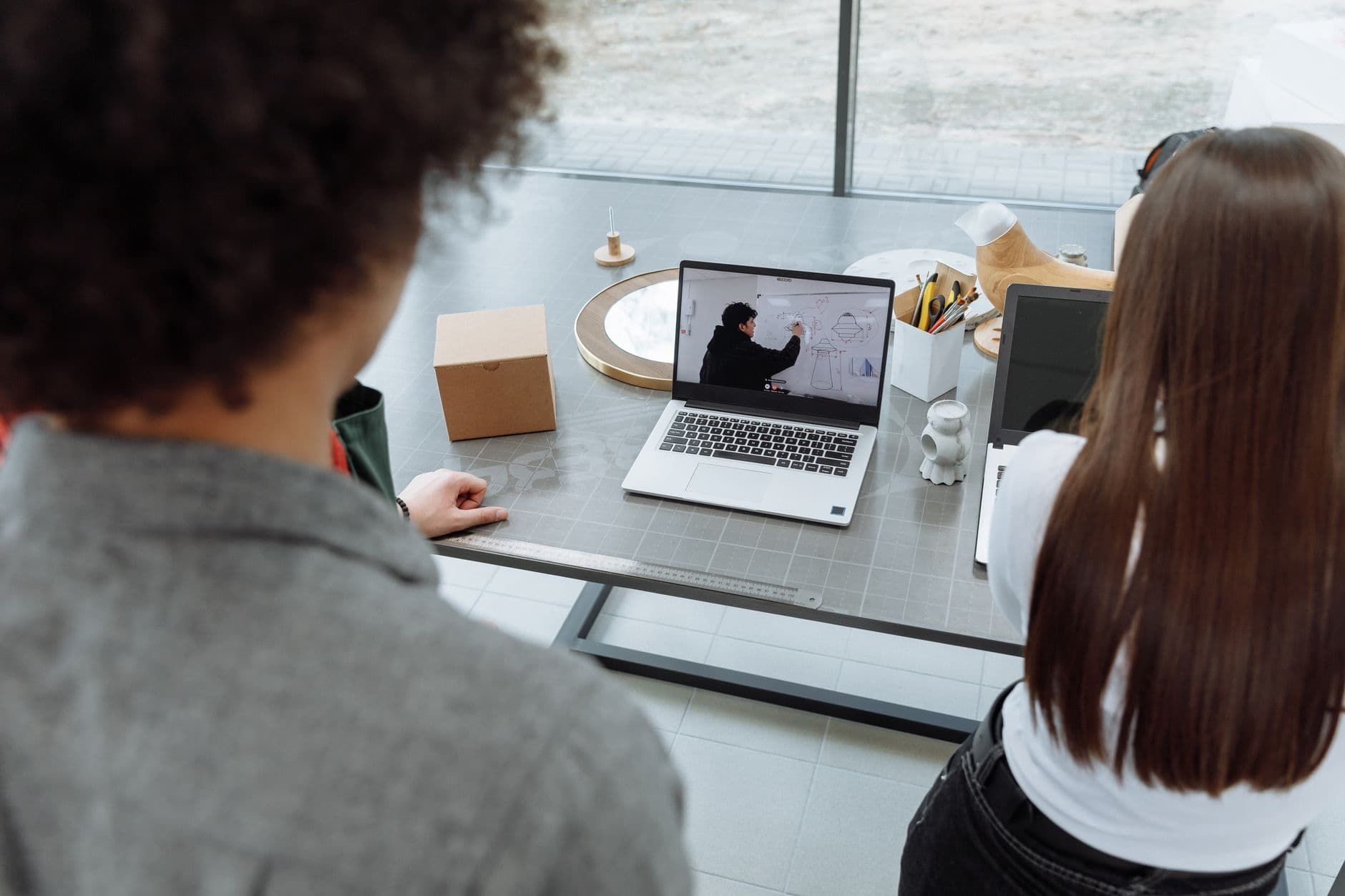 Google Workspace para trabalho remoto: vale a pena? Two colleagues engaging in a remote online meeting at a desk with a laptop.