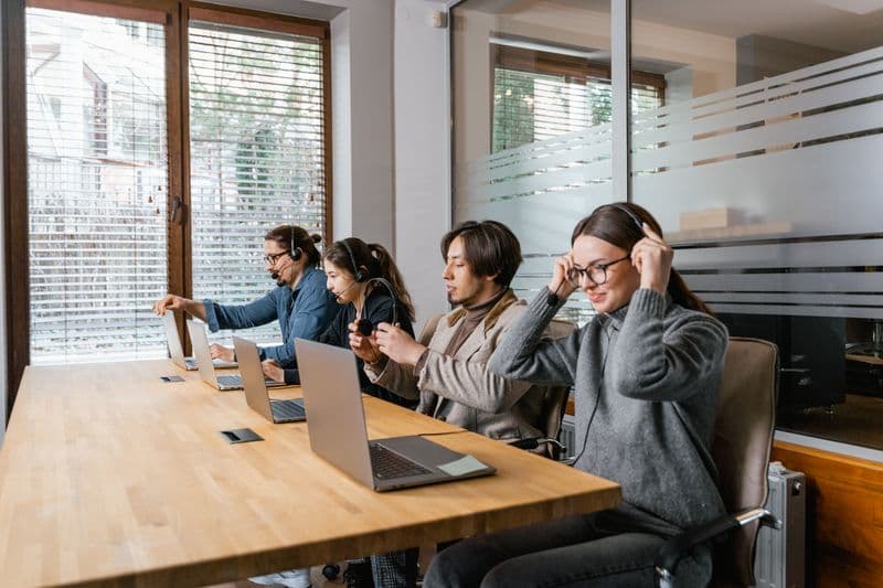 Home office para pessoa com deficiência: direitos e acessibilidade Professional team in a modern office setting using laptops and headsets for communication.