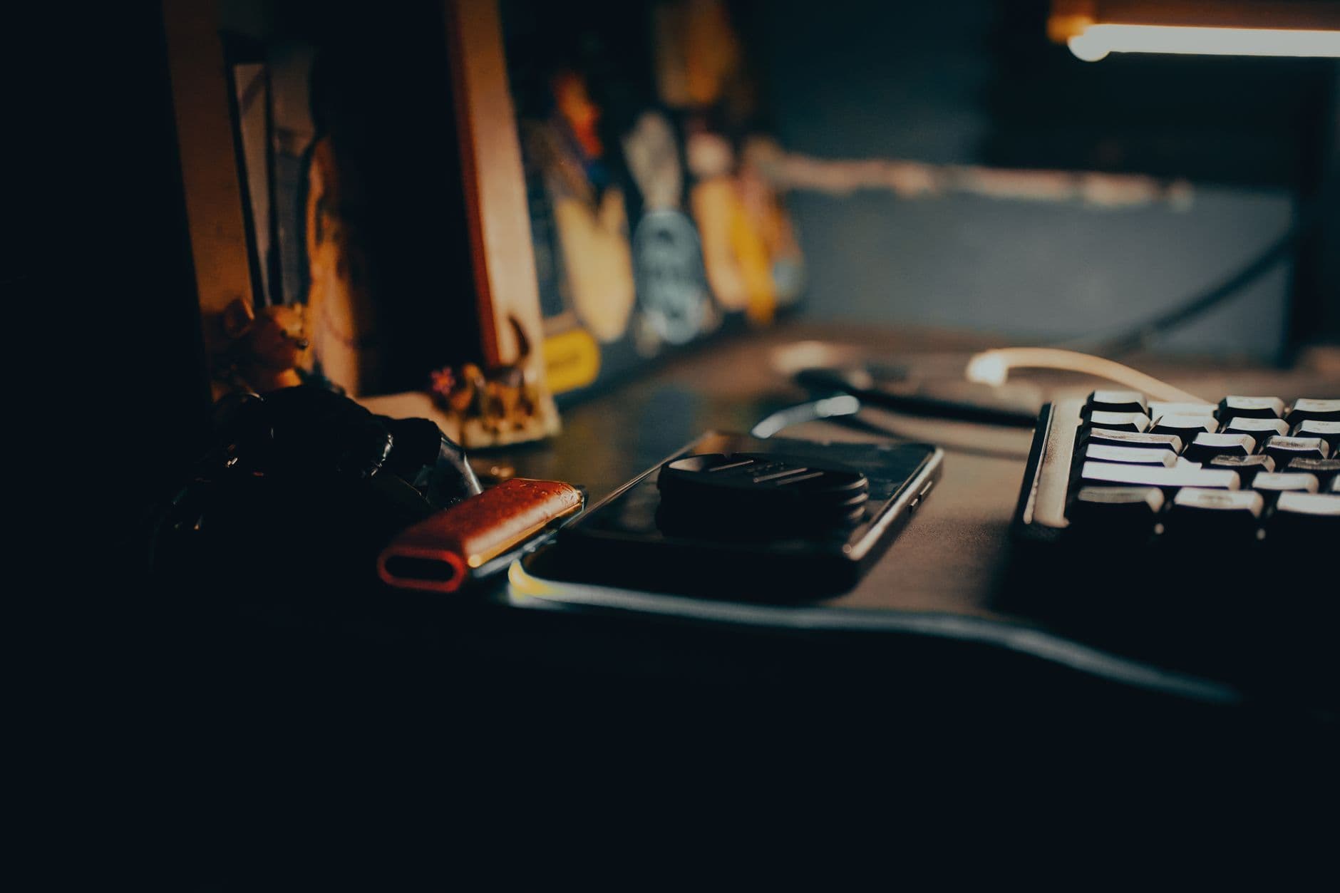 Home office pequeno: como aproveitar bem o espaço A dimly lit workspace featuring a keyboard, gadgets, and a warm ambient glow.