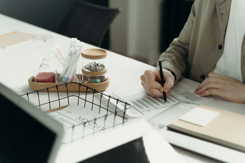 Horas extras no home office: como registrar corretamente A person writing on a document at a tidy desk with office supplies.