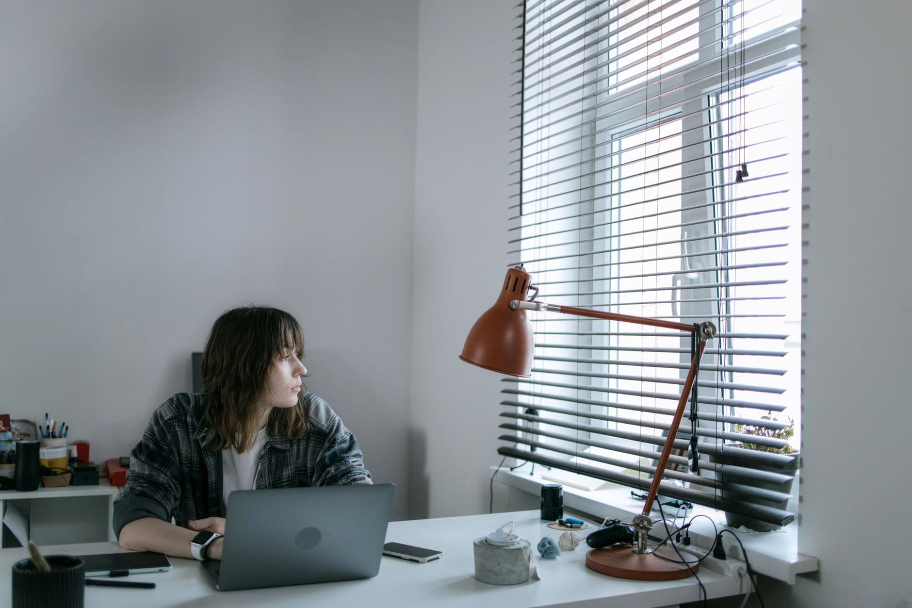 Pessoa trabalhando no home office com o rosto iluminado por uma janela e uma luminária de mesa.