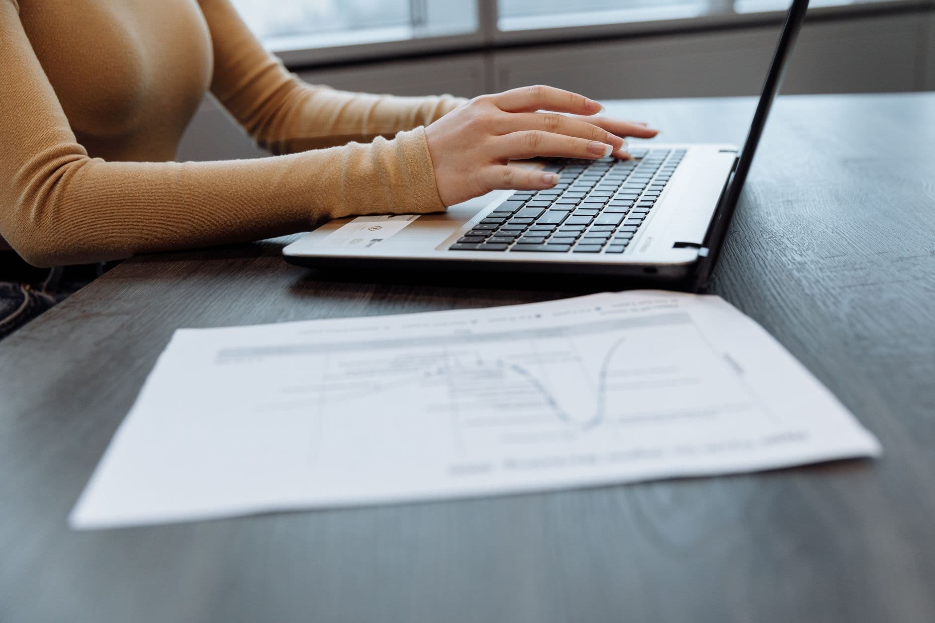 Freelancer conferindo documentos fiscais ao lado de um notebook em uma mesa de trabalho