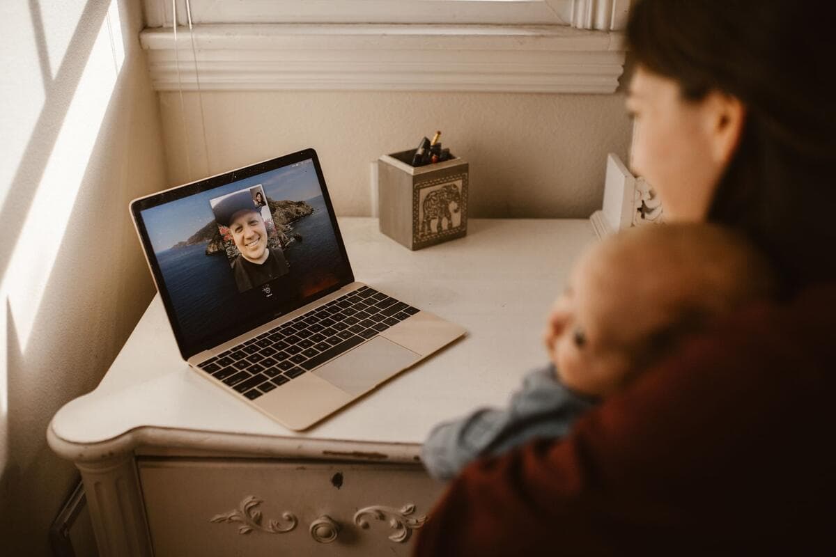 Mãe com bebê no colo participando de uma videochamada no notebook