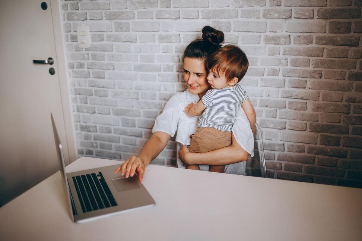 Mulher sorrindo para o notebook com o filho pequeno no colo, à mesa